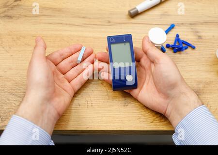 Vue du dessus photo de l'homme mains tenant une bande et glucomètre pour vérifier le niveau de sucre dans le sang à la maison, concept de diabète. Banque D'Images