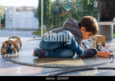 VYoung gamin jouant avec des trains de jouets sur le sol. Train à jouets semblable au train espagnol Cercanias Renfe et au train à grande vitesse AVE Banque D'Images