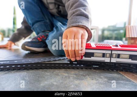 VYoung gamin jouant avec des trains de jouets sur le sol. Train à jouets semblable au train espagnol Cercanias Renfe et au train à grande vitesse AVE Banque D'Images