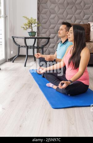 photo verticale d'un couple marié pratiquant le yoga sur un tapis dans leur salon Banque D'Images