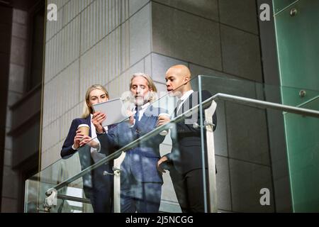 Les gens de l'entreprise multinationale et multiethnique de discuter affaires using digital tablet in modern office building, low angle view. Banque D'Images