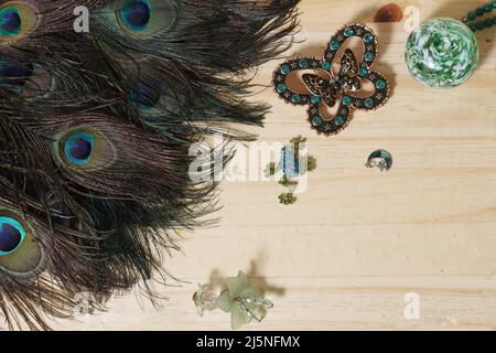 Plumes de paon avec perles vertes et brocher de papillons de cuivre et de vert sur table en bois Banque D'Images