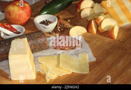 Salami au poivre sur plateau avec fromage anglais et irlandais, pommes en tranches et épices dans une cuisine rustique avec fenêtre de la cuisine Banque D'Images