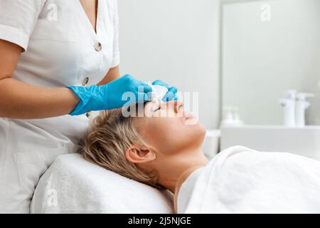 Un cosmétologue professionnel effectue un nettoyage mécanique profond du visage du client. Vue latérale. Concept de traitement de l'acné. Banque D'Images