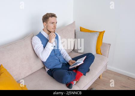 Homme d'affaires pensif assis sur un canapé avec un journal dans sa main, pense à des plans dans un costume de type à barbe bleu. Planifie sa routine quotidienne et ses réunions d'affaires. Concept de tenue de dossiers et de planification Banque D'Images