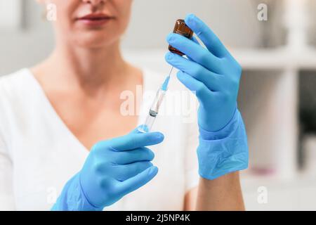 Un cosmétologue professionnel en gants médicaux bleus compose un médicament rajeunissant d'une ampoule dans une seringue. Gros plan des mains. Le concept de cosme Banque D'Images