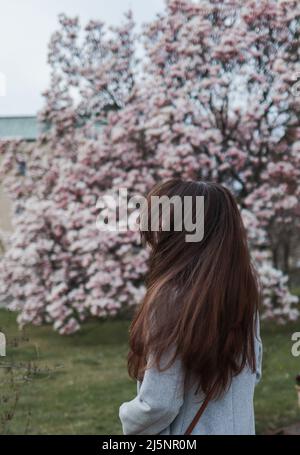 La jeune femme Brunette est debout près d'un magnifique gros magnolia rose. Banque D'Images