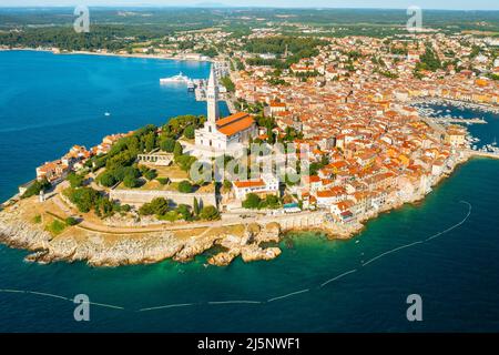 Le bateau à moteur naviguant autour de Rovinj. Environs de Rovinj et tour de l'église Saint-Euphemia. Les bâtiments de la ville croate près des forêts et de la mer Adriatique à la lumière du soleil. Panorama aérien Banque D'Images