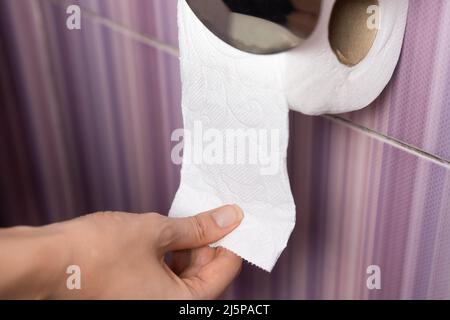 Gros plan de la main d'une femme tirant le papier toilette dans les toilettes sur un fond lilas. Banque D'Images