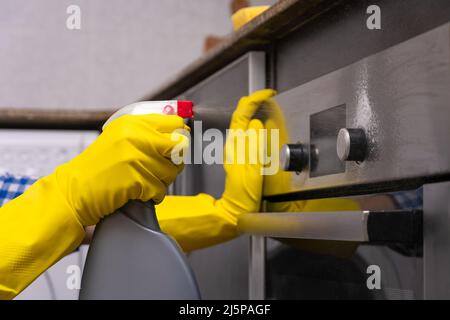 Les mains des femmes en gants de caoutchouc jaune frottent l'agent nettoyant sur la surface du four dans la cuisine. Concept de ménage et de ménage Banque D'Images
