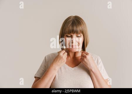Femme blonde senior en t-shirt posant et regardant vers le bas isolée sur le mur blanc Banque D'Images