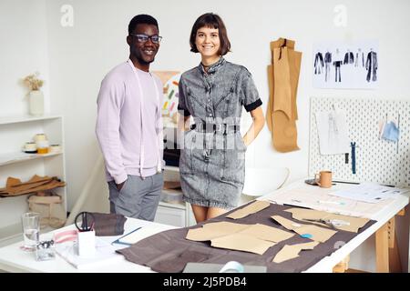 Une équipe multi-ethnique souriante de jeunes créateurs de mode travaillant sur un grand projet en atelier ou en studio Banque D'Images