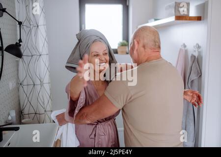 Couple senior amoureux dans la salle de bains, embrassant, concept de routine du matin. Banque D'Images