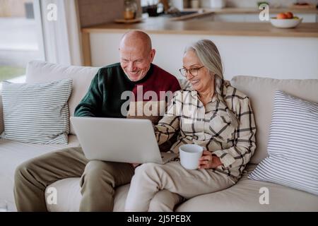 Couple senior assis sur un canapé et magasiner en ligne avec un ordinateur portable. Banque D'Images