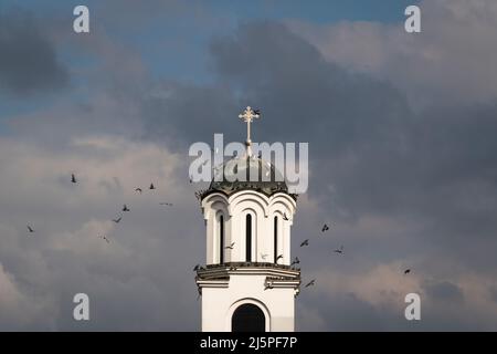 Un troupeau de pigeons survole le clocher de l'église contre des nuages sombres Banque D'Images