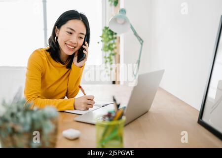 Femme parlant sur son téléphone mobile tout en travaillant avec un ordinateur portable à la maison. Banque D'Images