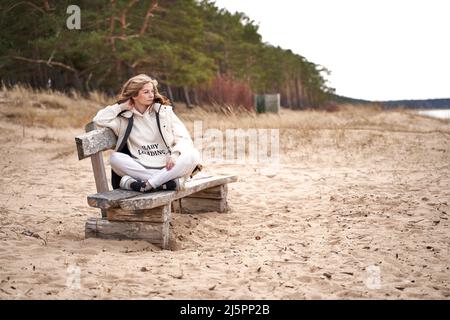 Femme enceinte avec texte bébé chargement sur le sweat à capuche blanc est assis sur le banc de bois à la mer Banque D'Images