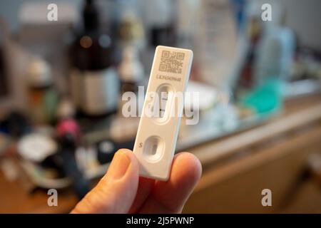 Détail d'une main tenant un test de débit latéral qui montre un résultat positif dans une chambre à coucher domestique, le 23rd avril 2022, à Londres, en Angleterre. Banque D'Images