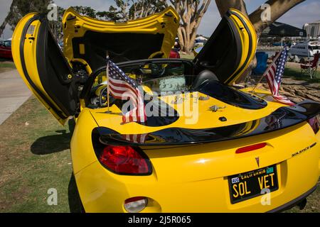 Voiture jaune Solstice, couverte de jouets de guerre et de drapeaux américains, dans une foire automobile vintage à San Diego Marina Banque D'Images