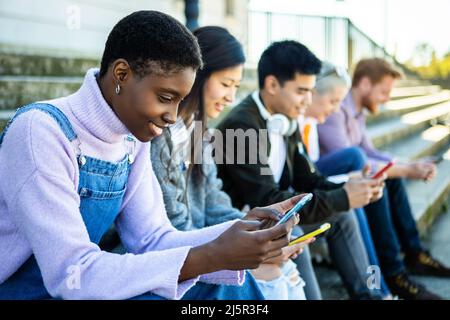 Jeunes souriants regardant le téléphone portable dans la rue de la ville Banque D'Images