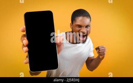 Homme américain africain émotionnel montrant un smartphone, mockup Banque D'Images