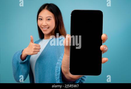 Femme asiatique montrant un smartphone avec écran vide et pouce vers le haut Banque D'Images