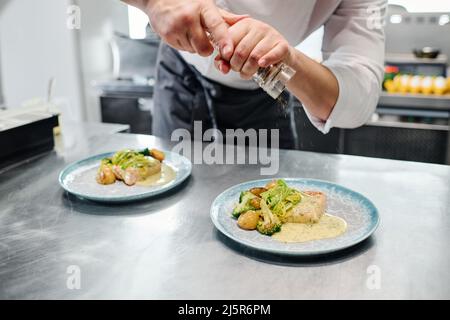 Gros plan du chef ajoutant des épices provenant d'un shaker sur les plats préparés sur la table avant de servir Banque D'Images