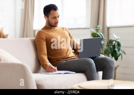 Portrait d'un homme arabe concentré à l'aide d'un ordinateur portable prenant des notes Banque D'Images