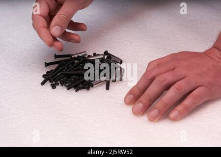 2 mains recherchant une vis noire sur un tas de boulons. Eléments de connexion pour l'industrie et l'artisanat. Banque D'Images