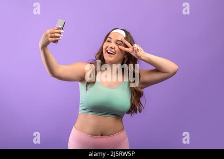 Joyeuse femme européenne plus de taille millénaire dans les vêtements de sport prenant le selfie au téléphone et le tournage en direct Banque D'Images