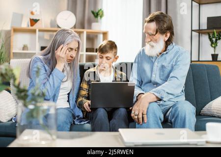 Petit-fils enseigner à un aîné de surfer sur Internet en utilisant l'ordinateur et la technologie et le style de vie moderne. Grand-parent caucasien heureux avec petit-enfant assis sur un canapé jouant à l'ordinateur portable ensemble à la maison Banque D'Images