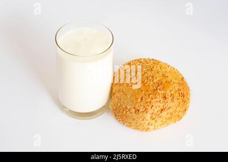 Un délicieux petit pain arrosé de graines de sésame se trouve à côté d'un verre de lait. Délicieux en-cas léger. Sur fond blanc, isolé Banque D'Images