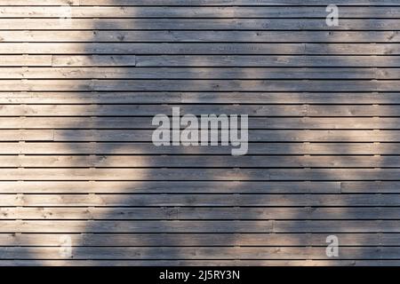 Planches en bois horizontales sur un mur. La lumière du soleil brille sur le bois et provoque des ombres. Une texture d'arrière-plan abstraite. Un bâtiment extérieur Banque D'Images