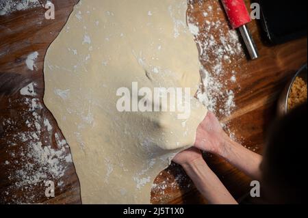 Vue de dessus des mains des femmes tirant et étirant une pâte vegan maison pour strudel ou tarte sur une table à manger. Banque D'Images