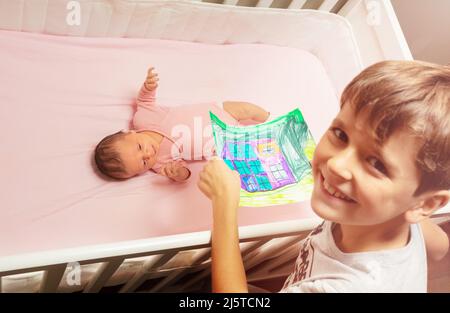 Un garçon souriant montre un dessin entre les mains de la petite fille de bébé Banque D'Images