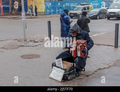 Dnepr, Ukraine - 02.10.2022: Un homme joue l'accordéon de bouton dans la rue en hiver. L'inscription en ukrainien pour le traitement du grand-daug Banque D'Images