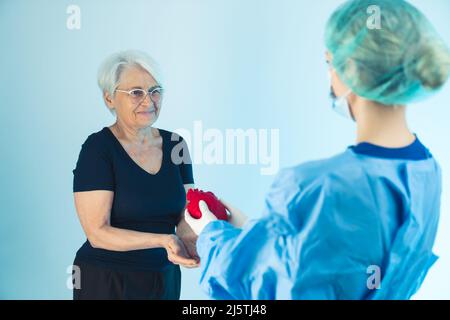 Médecin donnant un coeur rouge artificiel à une femme caucasienne senior studio shot moyen plan bleu fond de santé concept . Photo de haute qualité Banque D'Images