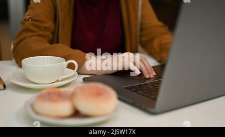 Image rognée, en gros plan, jeune femme travailleur utilisant un ordinateur portable, en tapant sur le clavier dans le bureau. Banque D'Images