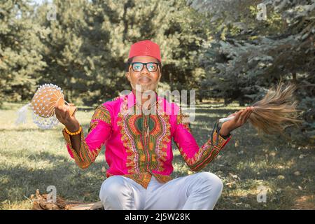 Le beau homme africain dans un costume national joue un tambour ethnique, djembe. Banque D'Images