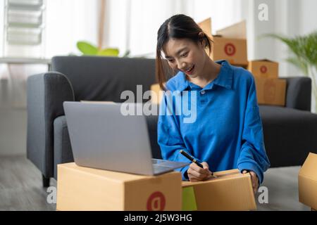 Expédition shopping en ligne, démarrage propriétaire de petite entreprise écrivant l'adresse sur boîte de carton au lieu de travail. Femme asiatique freelance petite entreprise Banque D'Images