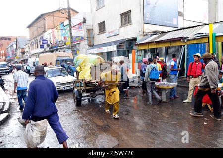 Un homme malgache tirant une voiturette dans un marché coloré à Antananarivo, Madagascar. Banque D'Images