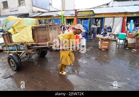 Un homme malgache tirant une voiturette dans un marché coloré à Antananarivo, Madagascar. Banque D'Images