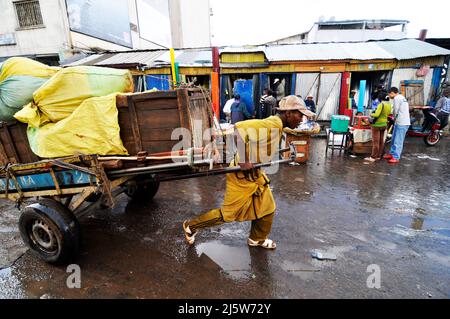 Un homme malgache tirant une voiturette dans un marché coloré à Antananarivo, Madagascar. Banque D'Images