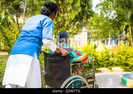 Vue arrière de l'infirmière emportant une femme âgée blessée en fauteuil roulant à pied dans le jardin de l'hôpital - concept de gardien, de traitement et de soins de santé. Banque D'Images