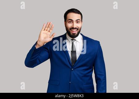 Jeune barbu satisfait se tenant debout et agité, regardant l'appareil photo avec un sourire ensanglant, portant un costume de style officiel. Prise de vue en studio isolée sur fond gris. Banque D'Images
