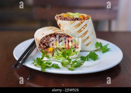 Burrito végétalien. Tranchez l'emballage des aliments crus avec des ingrédients végétaliens sur une assiette. Gros plan Banque D'Images