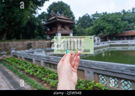 Vietnam 100 000 dong banknote en femme main sur la forteresse de Van Mieu fond. L'inverse du projet de loi dépeint l'ancienne forteresse vietnamienne de Van Banque D'Images