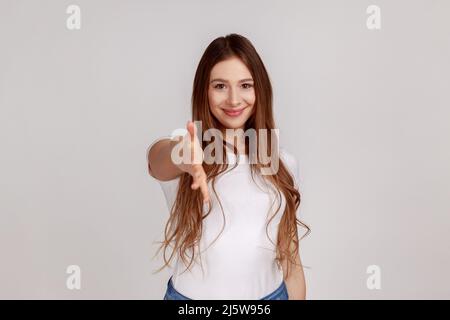 Permettez-moi de me présenter. Portrait d'une femme amicale qui donne la main à la poignée de main, saluant les clients avec un sourire crasseux, portant un T-shirt blanc. Prise de vue en studio isolée sur fond gris. Banque D'Images