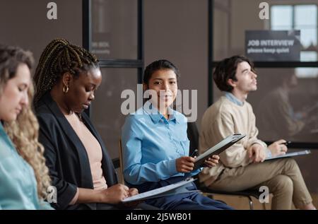 Portrait d'une jeune femme d'affaires avec un CV souriant à la caméra tout en attendant un entretien d'emploi avec d'autres candidats Banque D'Images