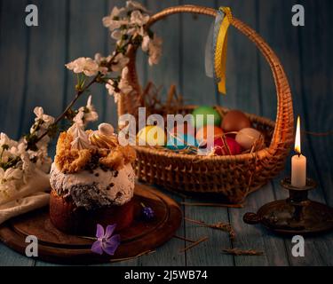 Compositio de Pâques. Gâteau de Pâques, un panier avec des œufs de couleur, un chandelier de bronze avec des bougies allumées et des fleurs printanières avec un fond flou. Banque D'Images